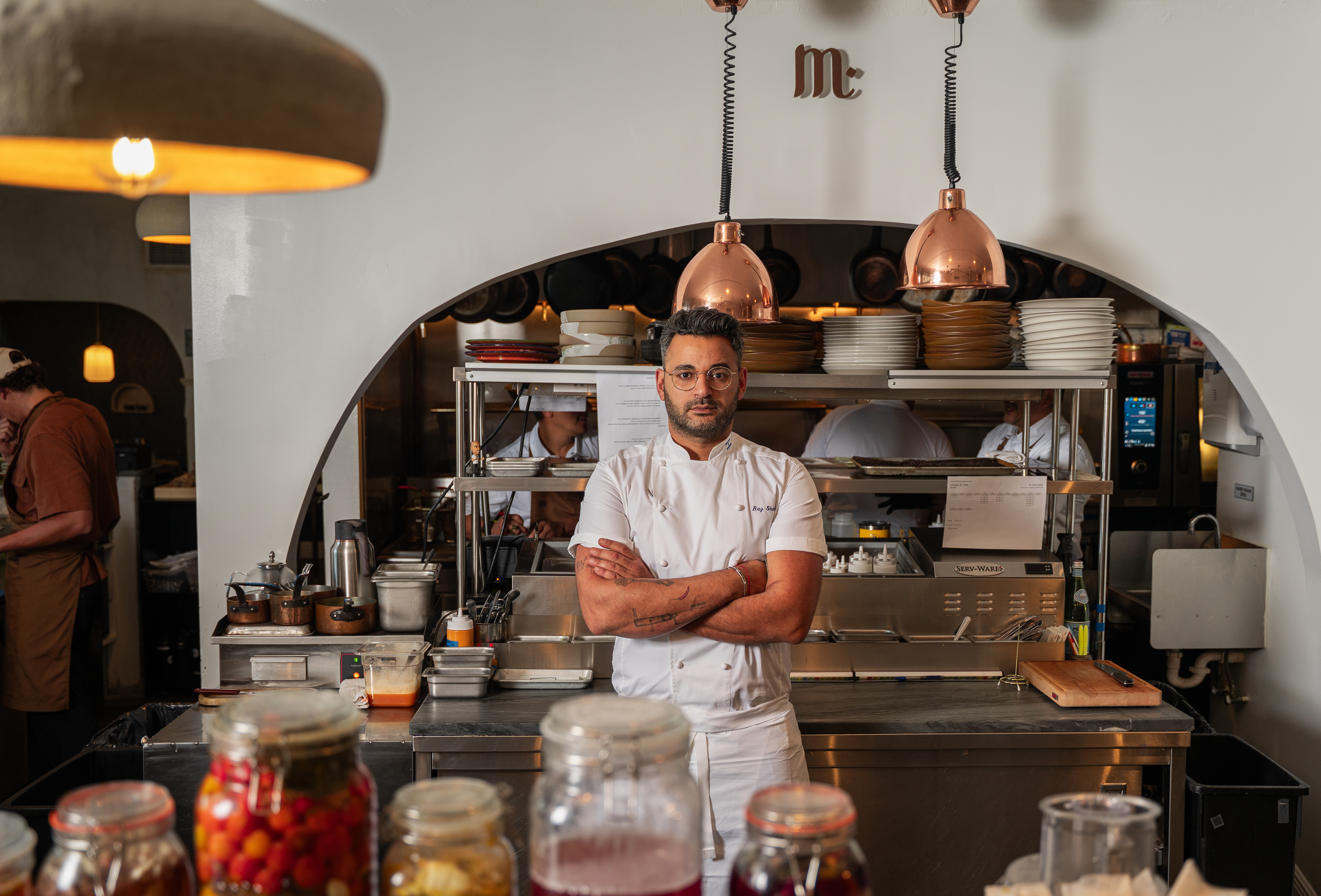 Chef portant une veste blanche, les bras croisés, dans la cuisine professionnelle de Mutra.